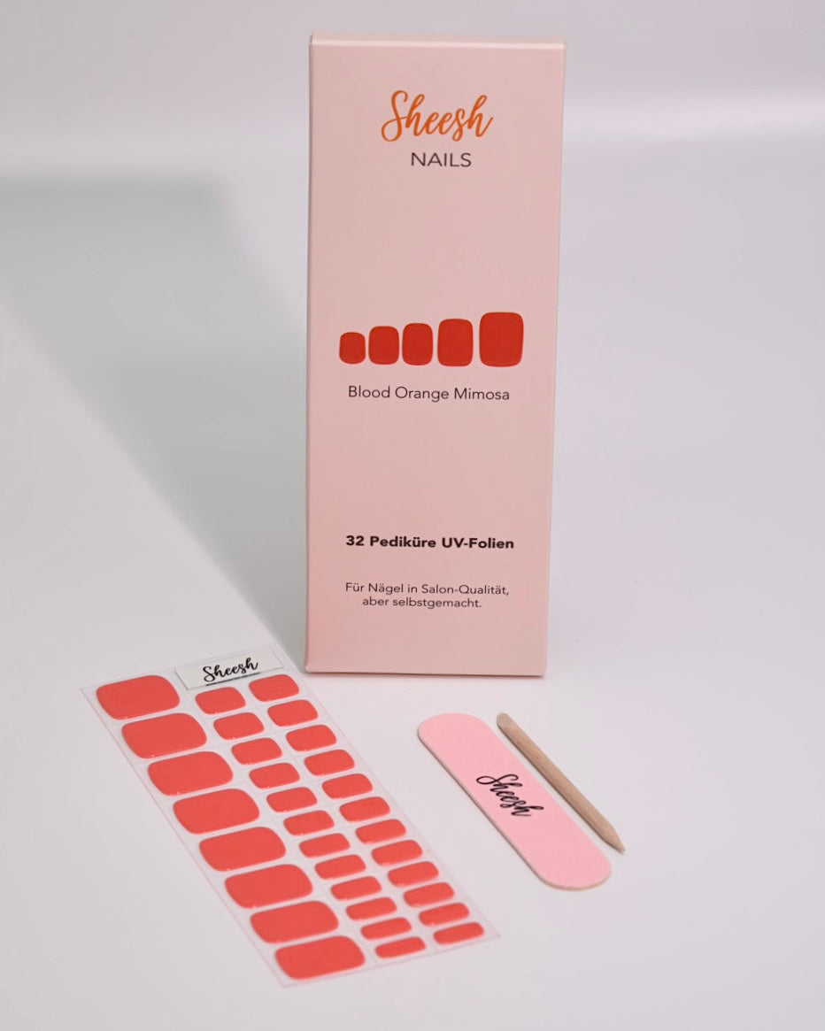 Produktaufnahme der Sheesh Nails Pedi UV-Nagelfolie „Blood Orange Mimosa“. Die Verpackung zeigt das elegante Design in Korallrot-Orange, kombiniert mit Feile und Folienbogen. Das Bild vermittelt Qualität, Frische und sommerliche Energie – ideal für eine moderne, gepflegte Pediküre im leuchtenden Statement-Look.