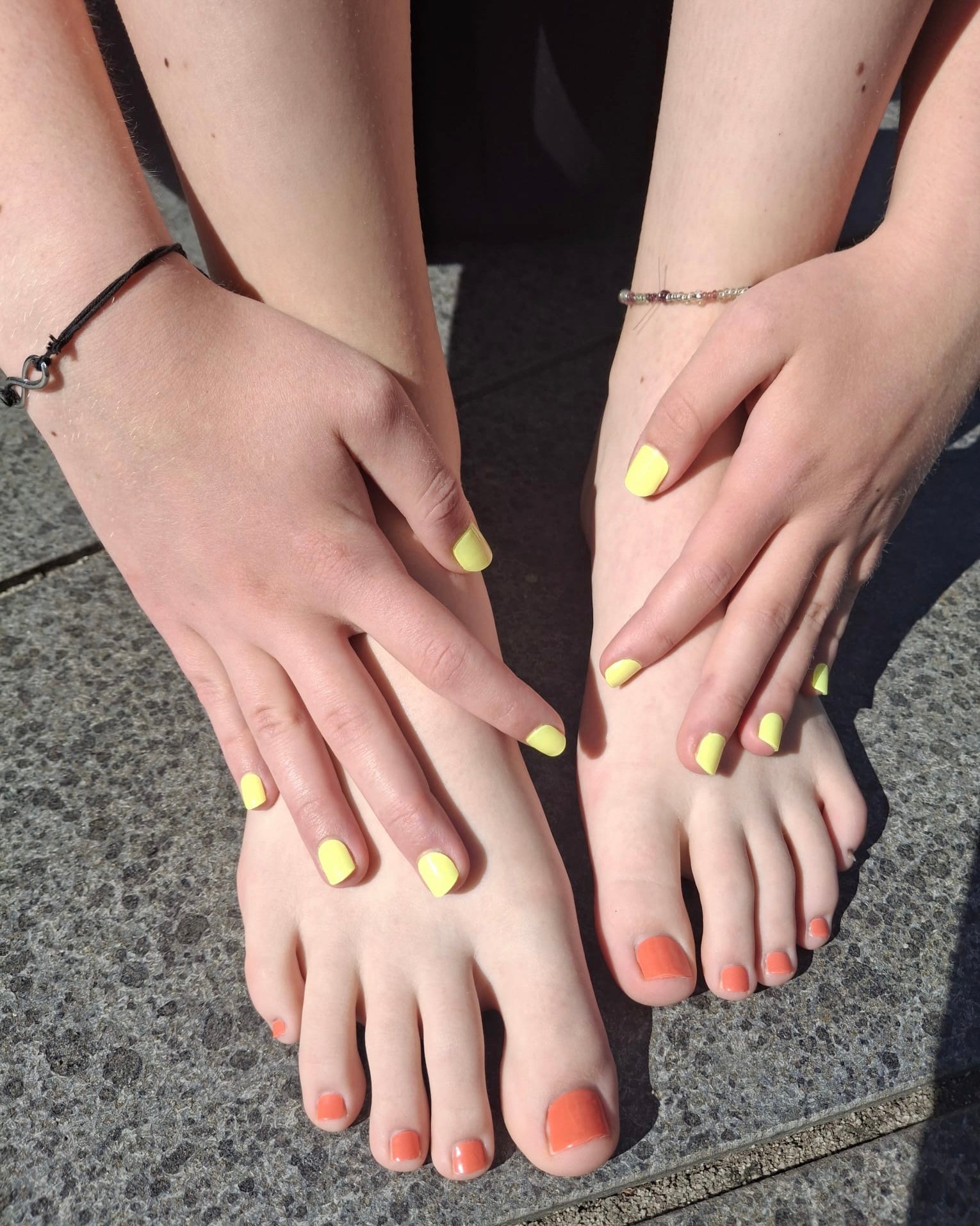 Sommerliche Aufnahme von Händen und Füßen mit Sheesh Nails Nagelfolien. Die Fingernägel leuchten in einem frischen Gelbton, während die Zehennägel in einem warmen Korallrot gestaltet sind. Der Look wirkt fröhlich, modern und ideal für sonnige Tage – perfekt für den Sommer und farbenfrohe Styles.