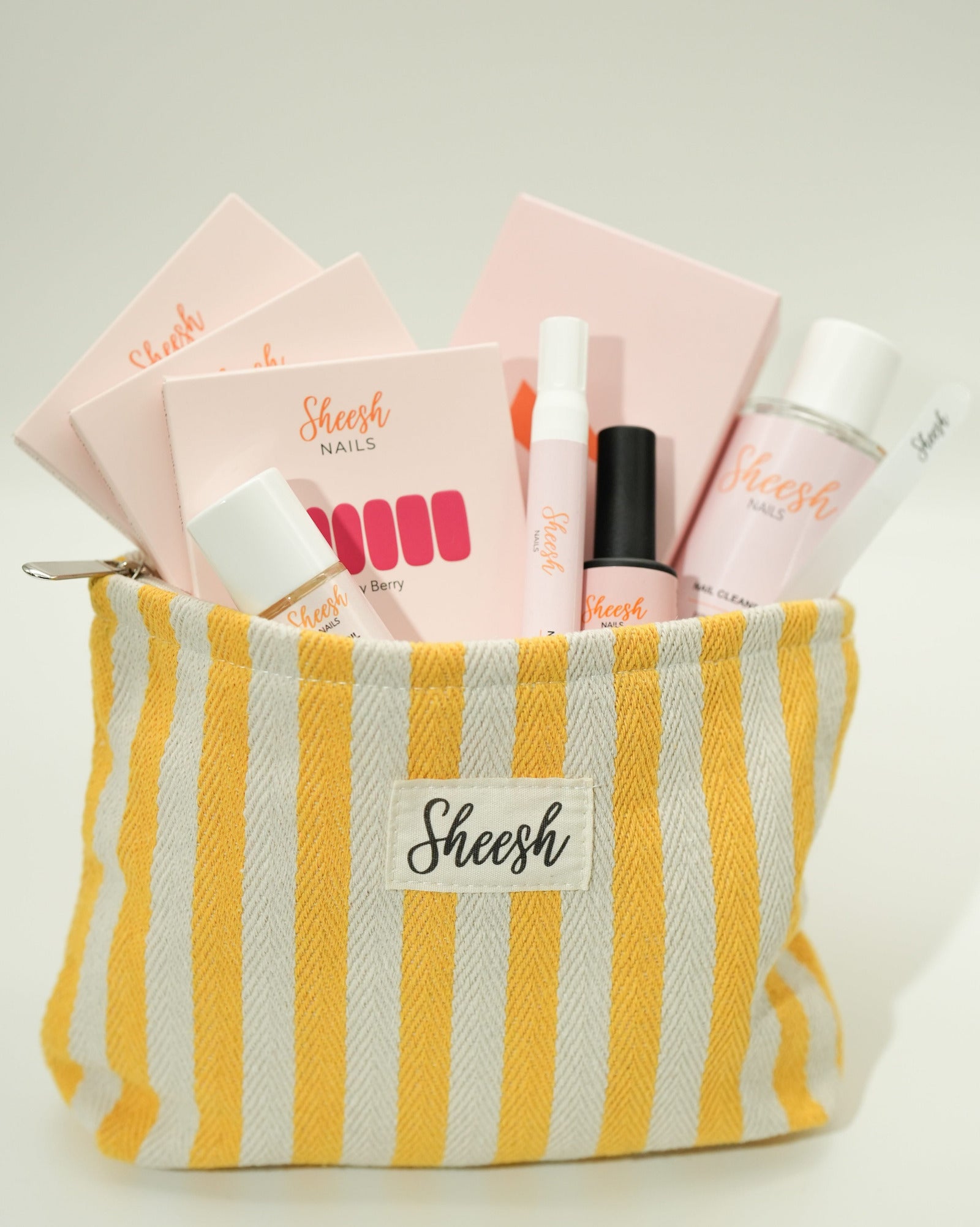 Produktfoto des Sheesh Nails Starter Sets mit Beauty Bag. Das Set enthält UV-Lampe, Top Coat, Nail Cleanser, Remover, Feile und Nagelfolien, verpackt in einer rosa-weiß gestreiften Sheesh Beauty Bag. Ideal für Einsteigerinnen in die Nagelfolien-Anwendung – alle wichtigen Tools für eine professionelle, langanhaltende Maniküre in einem Set.