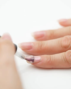 Nahaufnahme beim Auftragen des Sheesh Nails Top Coat „Glitter & Grit“. Der transparente Versiegelungslack mit feinem Schimmer sorgt für langanhaltenden Glanz, zusätzliche Haltbarkeit und ein elegantes Finish. Ideal zur Versiegelung von UV-Nagelfolien für ein professionelles, gepflegtes Nagelstyling.