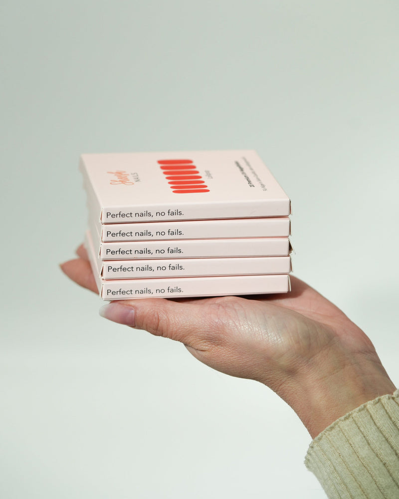Produktfoto eines 5er-Recharge-Sets der Sheesh Nails UV-Nagelfolien. Eine Hand hält fünf gestapelte Verpackungen mit der Aufschrift „Perfect nails, no fails“. Das Bild vermittelt Qualität und Professionalität – ideal zur Präsentation von Nachfüllsets oder Produktbündeln im Sortiment.