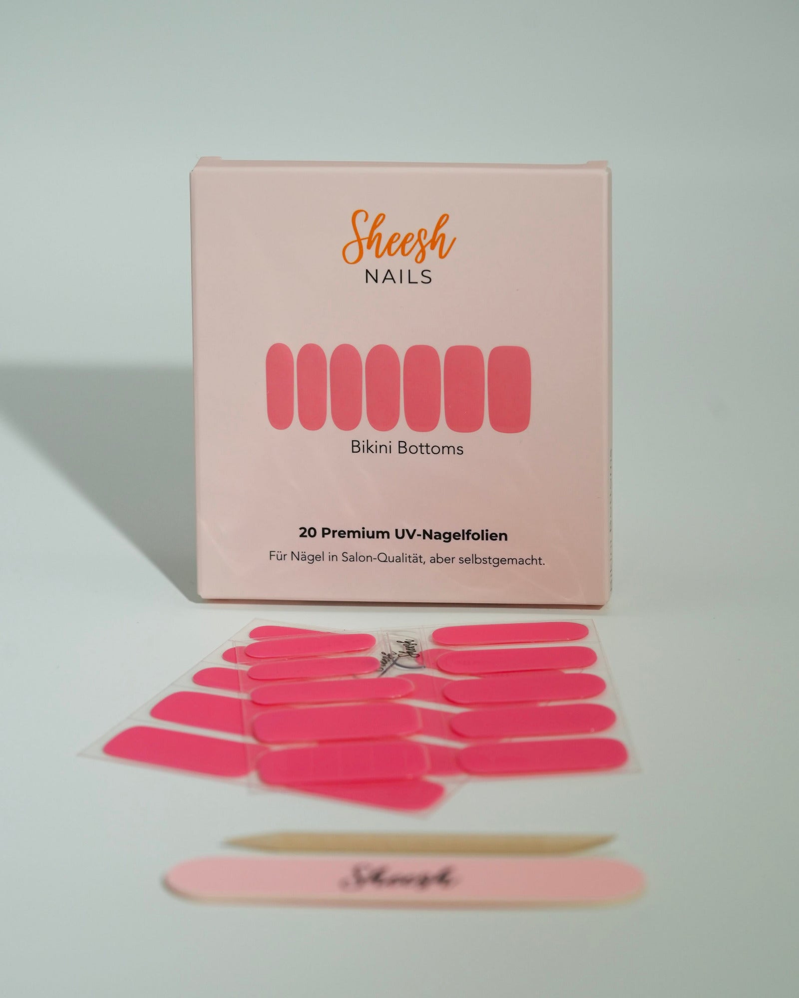 Produktfoto der Sheesh Nails UV-Nagelfolien „Bikini Bottoms“. Die selbstklebenden Folien in leuchtendem Pink sorgen für einen sommerlich-frischen Look in Salonqualität. Im Vordergrund liegen die geöffneten Folien und eine Sheesh-Nagelfeile – perfekt für auffällige, verspielte Maniküren mit Gute-Laune-Faktor.