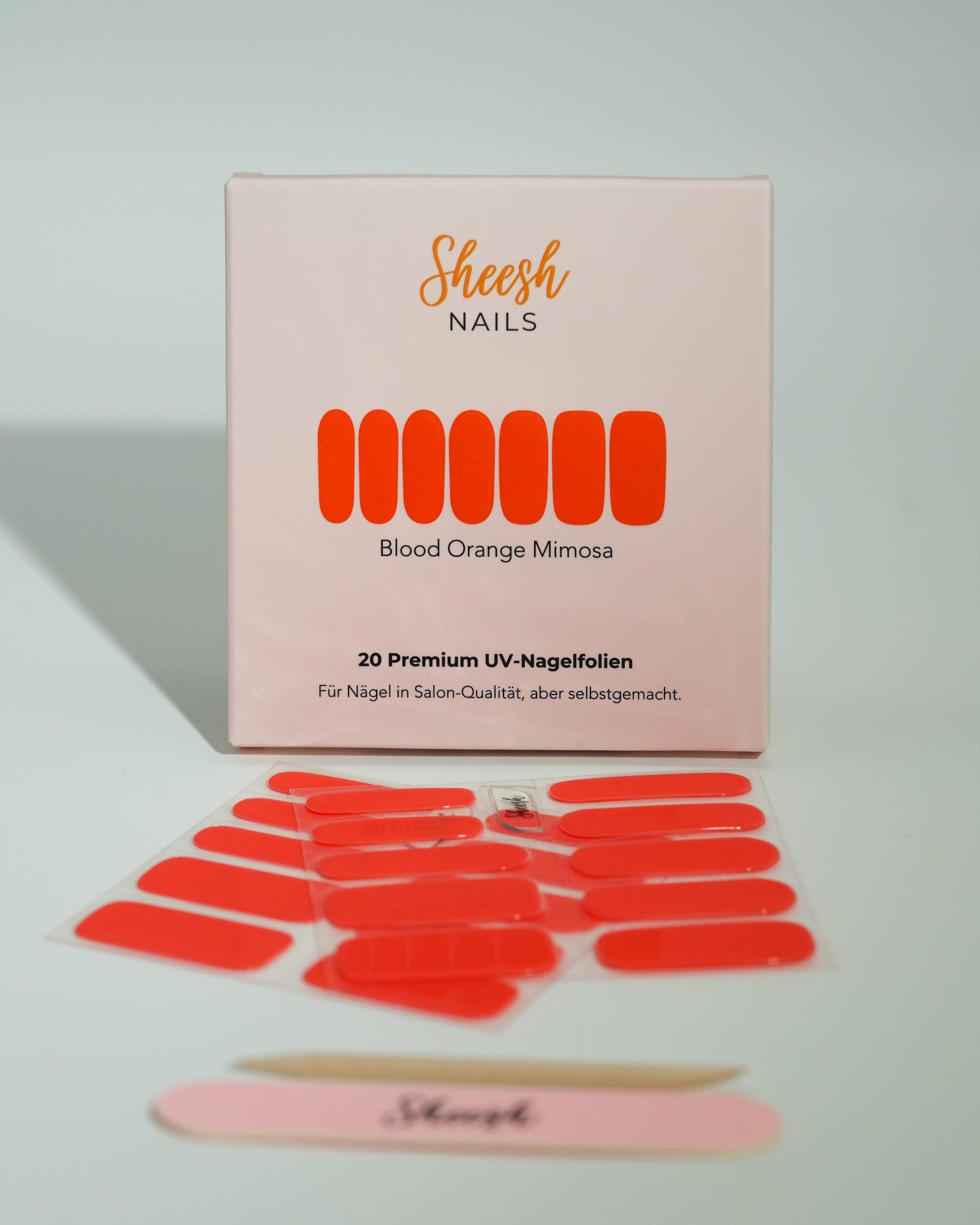 Produktfoto der Sheesh Nails UV-Nagelfolien „Blood Orange Mimosa“. Die selbstklebenden Folien in leuchtendem Orange setzen ein kräftiges Farbstatement und sorgen für einen sommerlich-frischen Look in Salonqualität. Im Vordergrund liegen die geöffneten Folien und eine Sheesh-Nagelfeile – ideal für auffällige, energiegeladene Maniküren mit Glanzfinish.