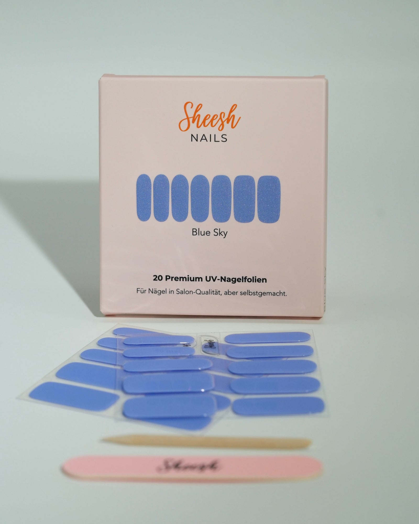 Produktfoto der Sheesh Nails UV-Nagelfolien „Blue Sky“. Die selbstklebenden Folien in hellem, glänzendem Blau verleihen den Nägeln einen frischen, modernen Look in Salonqualität. Im Vordergrund liegen die geöffneten Folien und eine Sheesh-Nagelfeile – perfekt für stilvolle, farbenfrohe Maniküren mit Sommerfeeling.