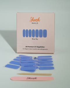 Produktfoto der Sheesh Nails UV-Nagelfolien „Blue Sky“. Die selbstklebenden Folien in hellem, glänzendem Blau verleihen den Nägeln einen frischen, modernen Look in Salonqualität. Im Vordergrund liegen die geöffneten Folien und eine Sheesh-Nagelfeile – perfekt für stilvolle, farbenfrohe Maniküren mit Sommerfeeling.