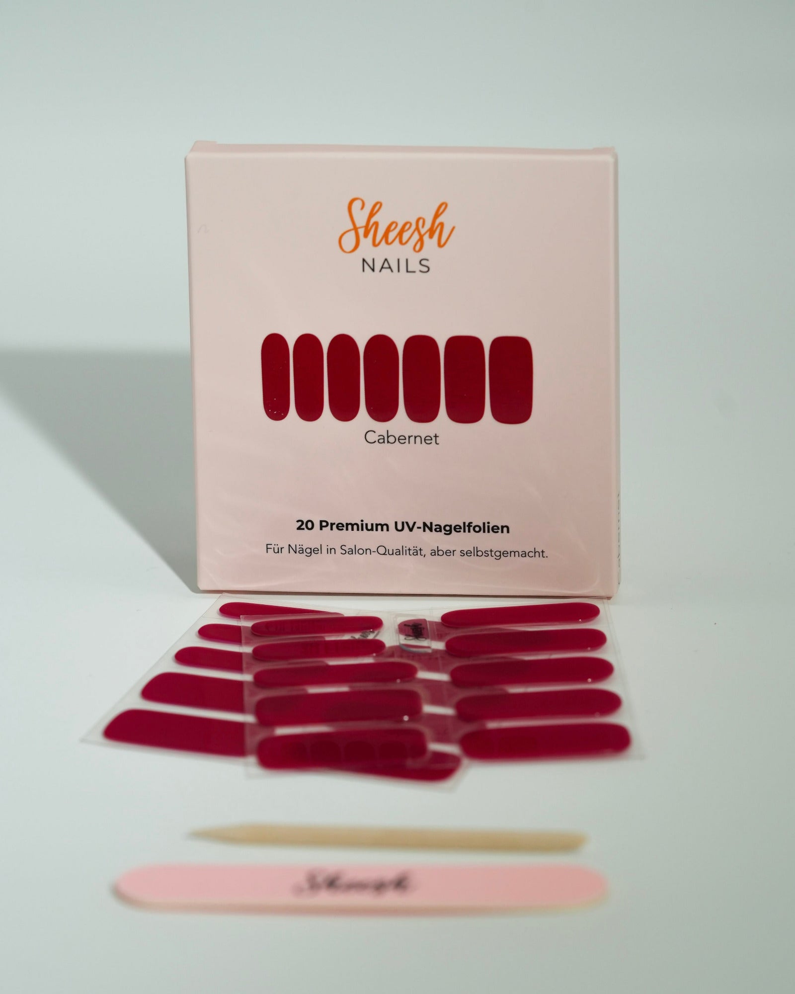 Produktfoto der Sheesh Nails UV-Nagelfolien „Cabernet“. Die selbstklebenden Folien in tiefem, glänzendem Rot verleihen den Nägeln einen luxuriösen, intensiven Look in Salonqualität. Im Vordergrund liegen die geöffneten Folien und eine Sheesh-Nagelfeile – perfekt für elegante, ausdrucksstarke Maniküren mit klassischem Charakter.