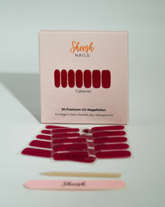 Produktfoto der Sheesh Nails UV-Nagelfolien „Cabernet“. Die selbstklebenden Folien in tiefem, glänzendem Rot verleihen den Nägeln einen luxuriösen, intensiven Look in Salonqualität. Im Vordergrund liegen die geöffneten Folien und eine Sheesh-Nagelfeile – perfekt für elegante, ausdrucksstarke Maniküren mit klassischem Charakter.