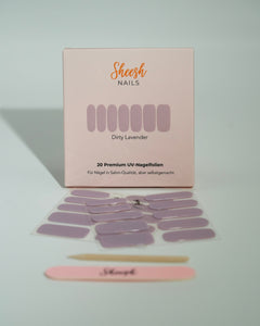 Produktfoto der Sheesh Nails UV-Nagelfolien „Dirty Lavender“. Die selbstklebenden Folien in mattem, dezentem Lavendelton verleihen den Nägeln einen modernen und eleganten Look in Salonqualität. Im Vordergrund liegen die geöffneten Folien und eine Sheesh-Nagelfeile – ideal für minimalistische, stilvolle Maniküren mit sanftem Farbakzent.