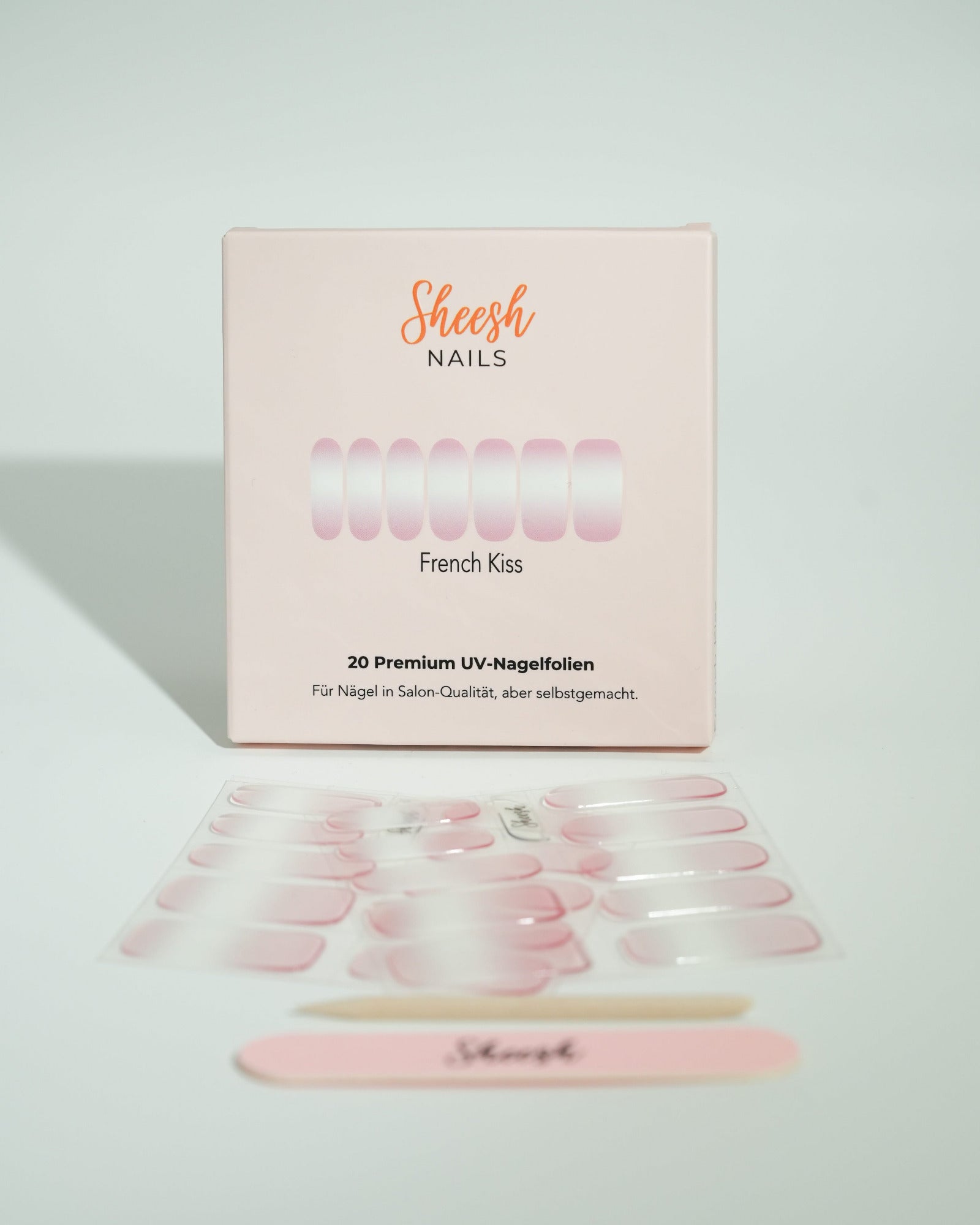 Produktfoto der Sheesh Nails UV-Nagelfolien „French Kiss“. Die selbstklebenden Folien zeigen ein klassisches French-Maniküre-Design mit zartrosa Grundton und weißer Nagelspitze für einen eleganten, gepflegten Look in Salonqualität. Im Vordergrund liegen die geöffneten Folien und eine Sheesh-Nagelfeile – ideal für zeitlose, feminine Maniküren mit Glanzfinish.