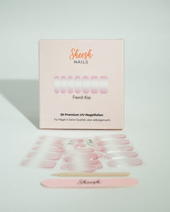 Produktfoto der Sheesh Nails UV-Nagelfolien „French Kiss“. Die selbstklebenden Folien zeigen ein klassisches French-Maniküre-Design mit zartrosa Grundton und weißer Nagelspitze für einen eleganten, gepflegten Look in Salonqualität. Im Vordergrund liegen die geöffneten Folien und eine Sheesh-Nagelfeile – ideal für zeitlose, feminine Maniküren mit Glanzfinish.