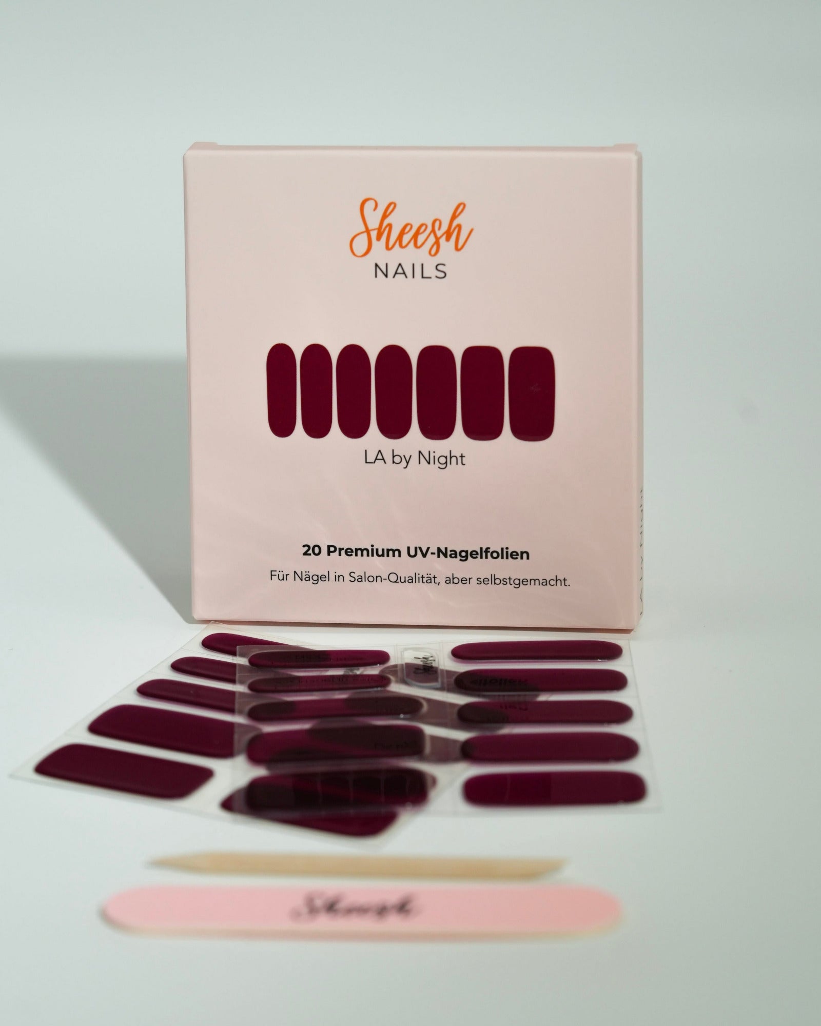 Produktfoto der Sheesh Nails UV-Nagelfolien „LA by Night“. Die selbstklebenden Folien in elegantem Dunkelrot verleihen den Nägeln einen tiefen, glänzenden Look in Salonqualität. Im Vordergrund liegen die geöffneten Folien und eine Sheesh-Nagelfeile – ideal für edle, ausdrucksstarke Maniküren mit Glamour-Effekt.