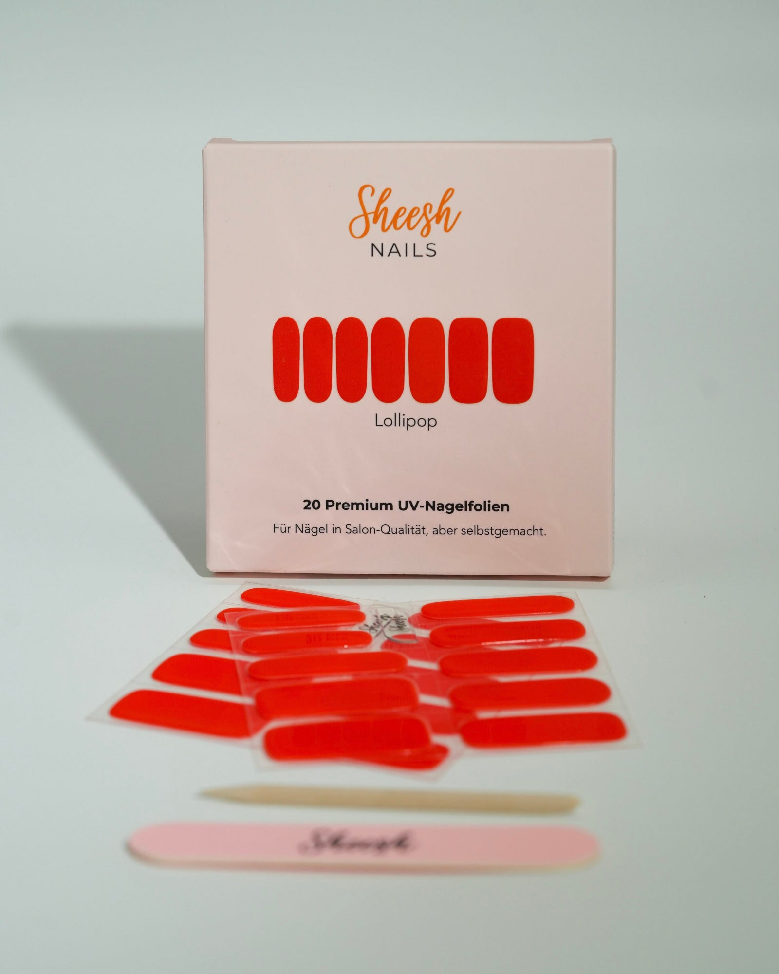 Produktfoto der Sheesh Nails UV-Nagelfolien „Lollipop“. Die selbstklebenden Folien in kräftigem Rot verleihen den Nägeln einen auffälligen, hochglänzenden Look in Salonqualität. Im Vordergrund liegen die geöffneten Folien und eine Sheesh-Nagelfeile – perfekt für energiegeladene, moderne Maniküren mit Statement-Farbe.