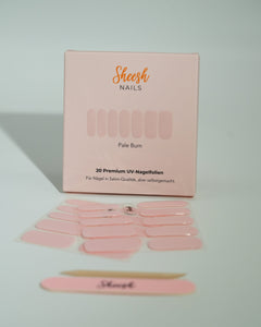 Produktfoto der Sheesh Nails UV-Nagelfolien „Pale Bum“. Die selbstklebenden Folien in dezentem Nude-Ton verleihen den Nägeln einen eleganten, natürlichen Look in Salonqualität. Im Vordergrund liegen die geöffneten Folien und eine Sheesh-Nagelfeile – ideal für gepflegte, minimalistische Maniküren mit sanftem Glanz.