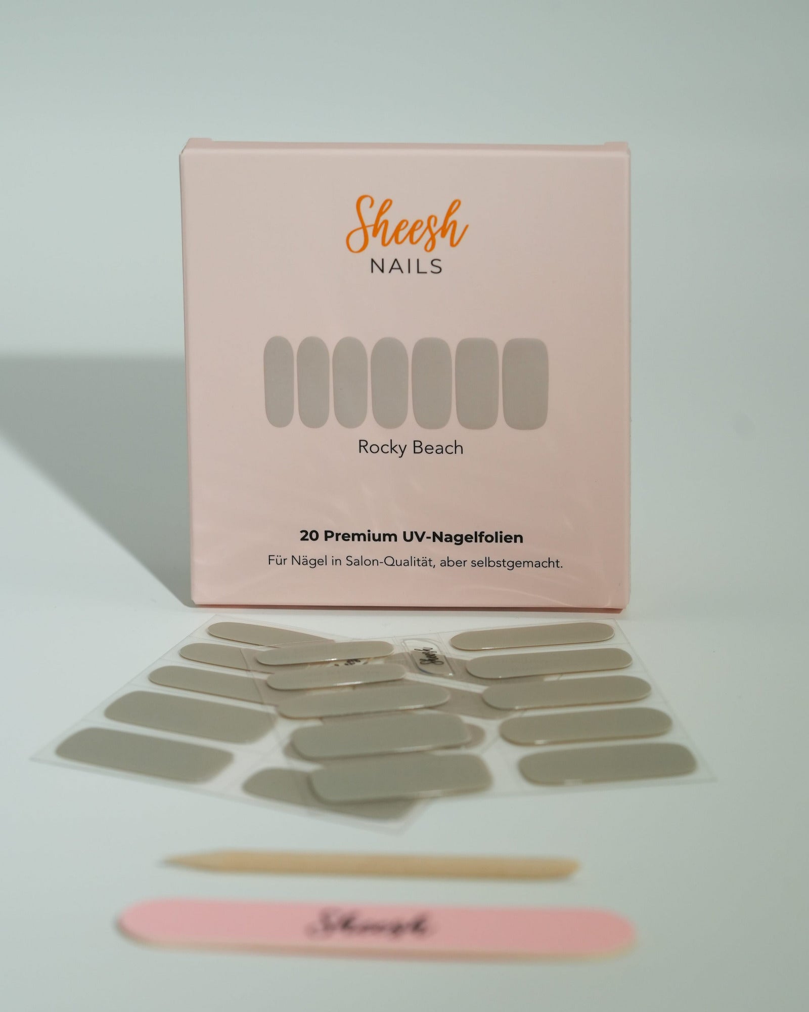 Produktfoto der Sheesh Nails UV-Nagelfolien „Rocky Beach“. Die selbstklebenden Folien in elegantem Beige verleihen den Nägeln einen natürlichen, glänzenden Look in Salonqualität. Im Vordergrund liegen die geöffneten Folien und eine Sheesh-Nagelfeile – ideal für dezente, gepflegte Maniküren mit modernem Touch.