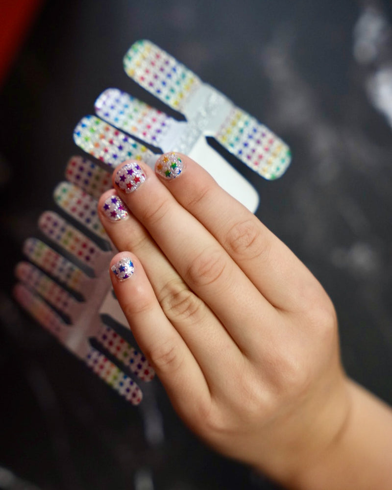 SHEESH Nails – Stars | Kinder-Nagelfolien, Bild 02: Kinderhand hält bunte Glitzer-Nagelfolien mit Regenbogen-Sternchen von – fröhliches Naildesign für Kinder….