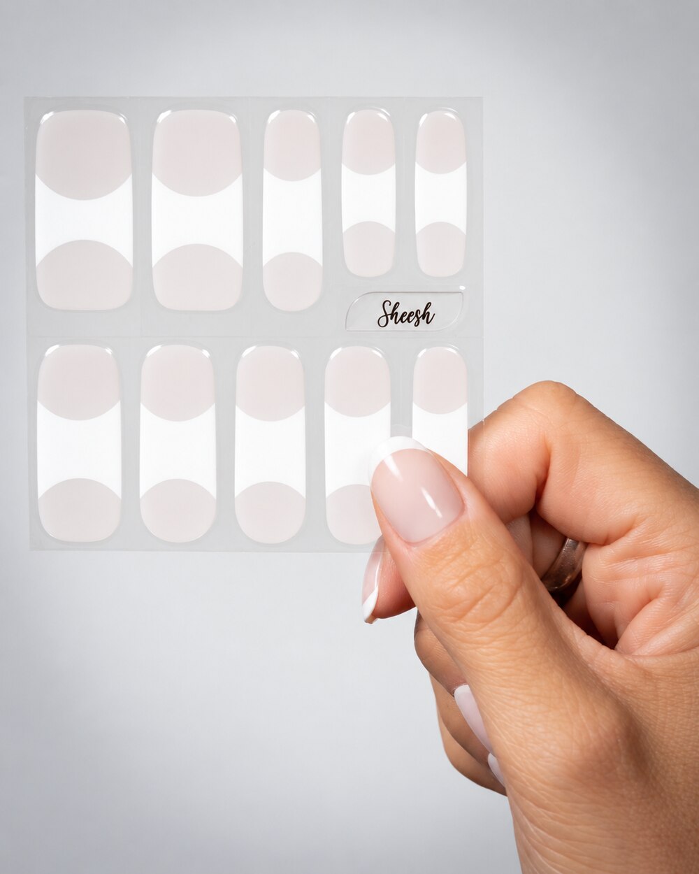 SHEESH Nails – Timeless UV-Nagelfolien, Bild 01: Folienbogen im Milky-French-Look mit breiten weißen Spitzen in einer Hand.