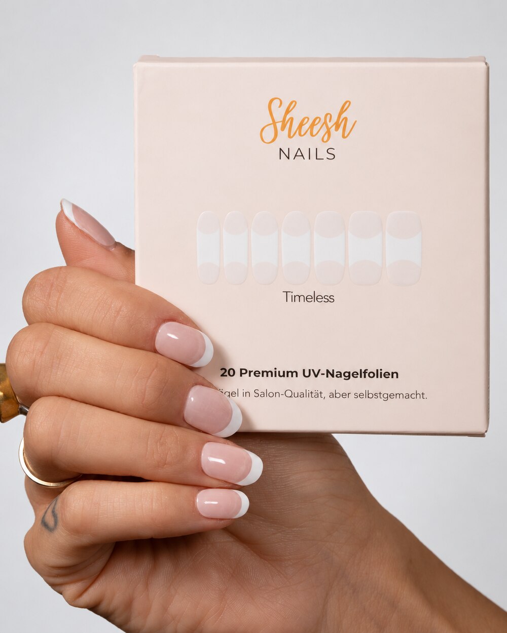 SHEESH Nails – Timeless UV-Nagelfolien, Bild 04: Timeless-Verpackung vor einer Hand mit French-Maniküre.