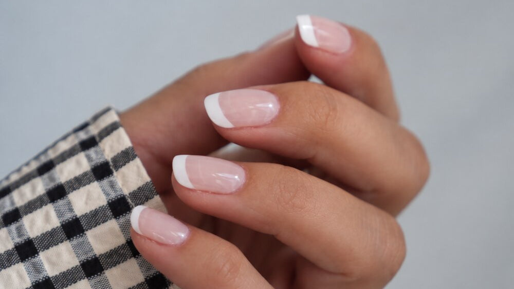 SHEESH Nails – Timeless UV-Nagelfolien, Bild 05: French-Nägel an einer Hand mit schwarz-weiß kariertem Ärmel.