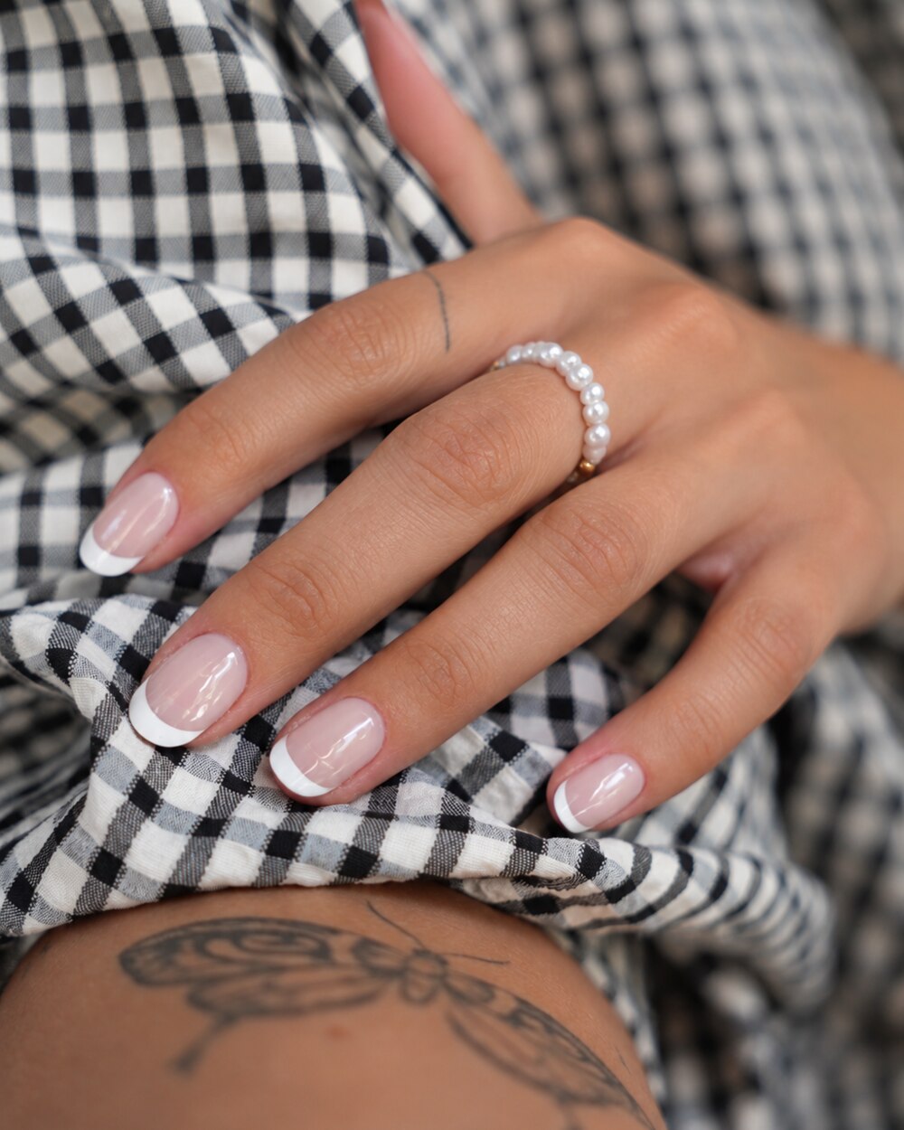 SHEESH Nails – Timeless UV-Nagelfolien, Bild 07: Nahaufnahme der getragenen French-Nägel mit Perlenring und kariertem Stoff.