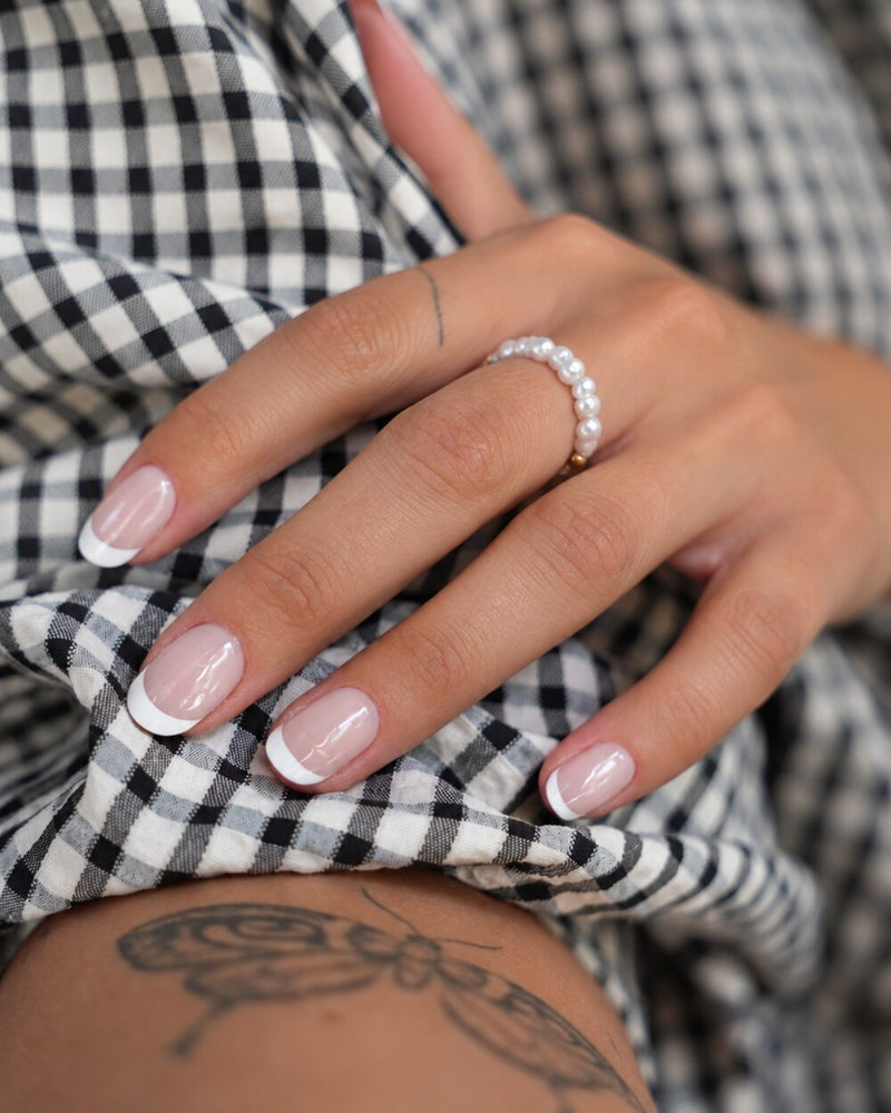 SHEESH Nails – Timeless UV-Nagelfolien, Bild 07: Nahaufnahme der getragenen French-Nägel mit Perlenring und kariertem Stoff.